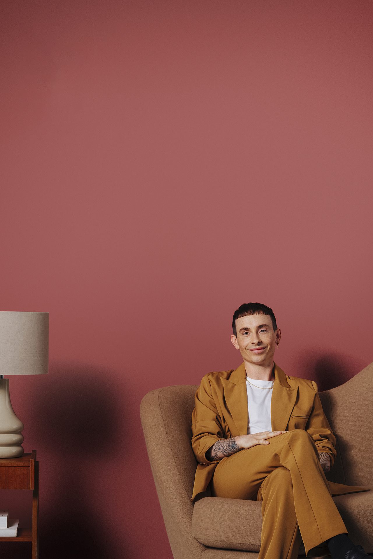 man sat on sofa next to side table in front of red wall
