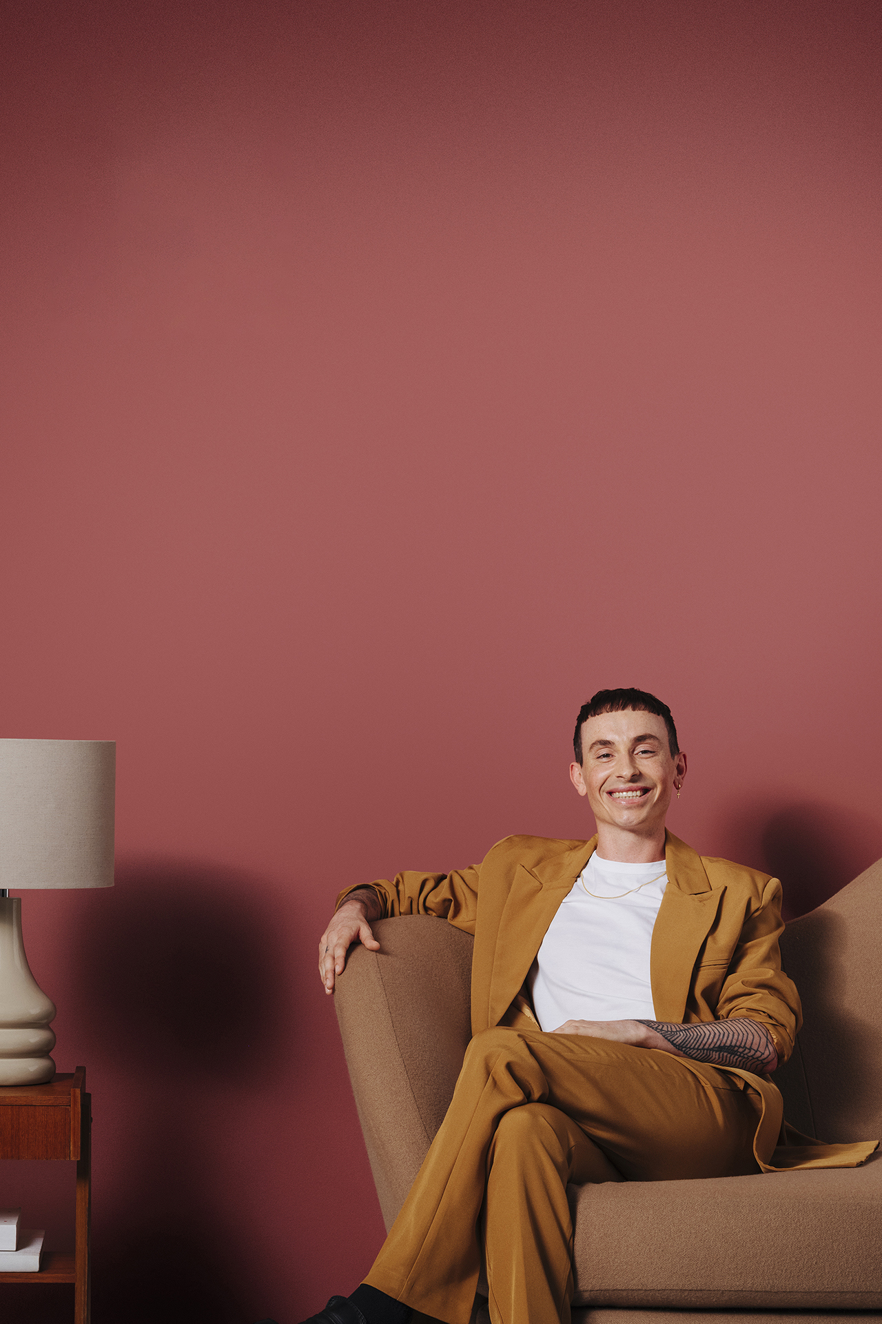 man sat on sofa next to side table in front of red wall