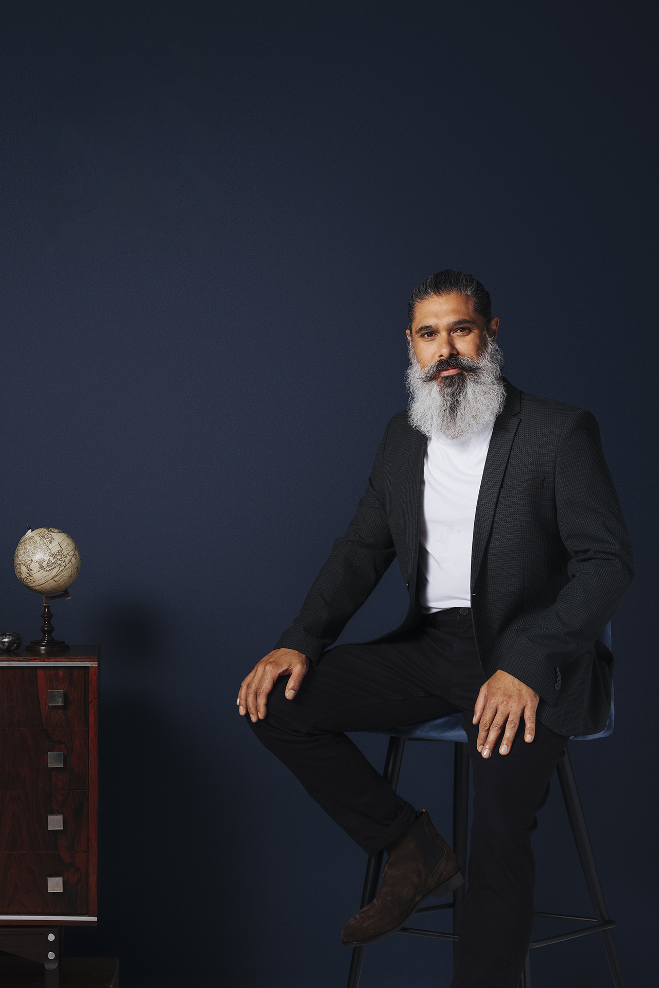 man sat next to side table with globe in front of navy blue wall